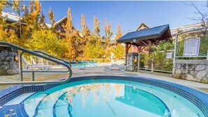 A swimming pool with a stone wall and a wooden gazebo in the background. - Luxury ski-in/out | Complex pool, hot tub & gym | BBQ (Whistler)