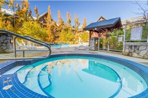 Ein Schwimmbecken mit einer Steinmauer und einem hölzernen Pavillon im Hintergrund.