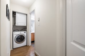 A laundry room with a washing machine and dryer, a white door, and a hallway leading to a bathroom. - AC in bedrooms | Private hot tub | Pets | Location (Whistler)