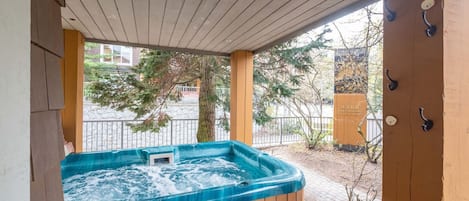 A wooden hot tub under a covered porch with a view of a street and trees.