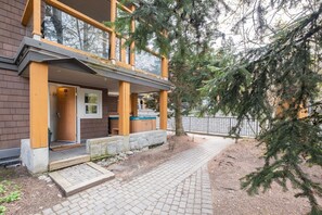 A two-story building with a covered porch, a stone pathway, and a metal fence. - AC in bedrooms | Private hot tub | Pets | Location (Whistler)
