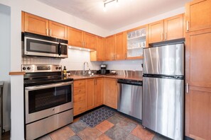 A modern kitchen with wooden cabinets, stainless steel appliances, and a tiled floor. - AC in bedrooms | Private hot tub | Pets | Location (Whistler)