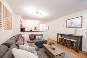 A modern living room with a sectional sofa, a wooden coffee table, and a dining area with a bench. - Beautiful 2BDR townhouse | Private hot tub | Pets (Whistler)