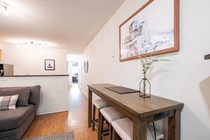 Ein modernes Wohnzimmer mit einem Holzesstisch, einer Couch und einer Küche im Hintergrund.