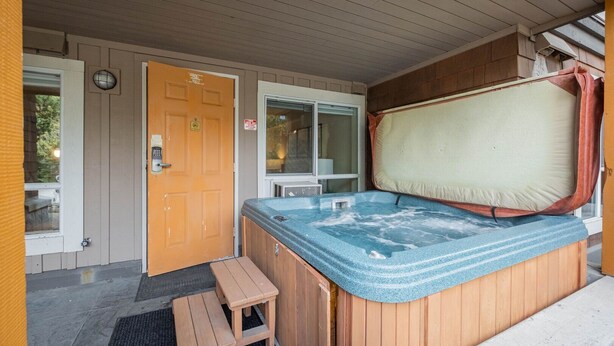 Un bain à remous avec une terrasse en bois, une porte dotée d’un judas et un petit banc en bois.