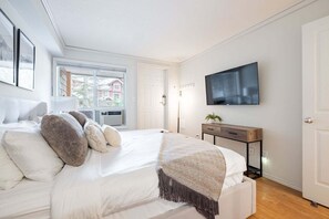 A bedroom with a large bed, a TV mounted on the wall, and a window with a view of buildings outside. - Beautiful 2BDR townhouse | Private hot tub | Pets (Whistler)