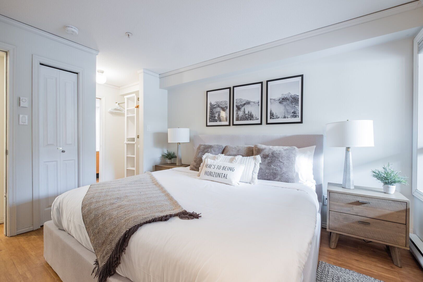 A bedroom with a bed, bedside tables, a nightstand, a lamp, a wall-mounted shelf, and a door.