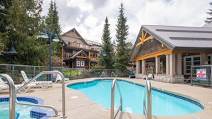 Une piscine dotée d’un poste de surveillance pour les sauveteurs, de chaises longues et d’un bâtiment à la façade en bois.