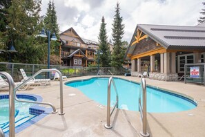 A swimming pool with a lifeguard stand, lounge chairs, and a building with a wooden facade. - Beautiful 2BDR townhouse | Private hot tub | Pets (Whistler)