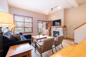 A living room with a fireplace, a TV mounted above it, a sofa, a coffee table, and a dining table. - Private Hot Tub | BBQ | Free parking | Ski-in/out (Whistler)