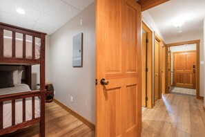 A room with a bunk bed, a wooden door, a small table, and a wall-mounted air conditioning unit. - Private Hot Tub | BBQ | Free parking | Ski-in/out (Whistler)