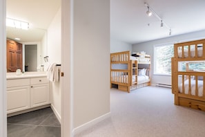 A bedroom with bunk beds, a window, and a bathroom with a mirror and cabinets. - Large deck | Private Hot Tub | BBQ | Pet friendly (Whistler)