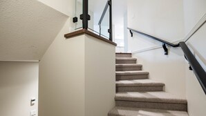 Una escalera alfombrada con barandilla de vidrio y pasamanos de madera.