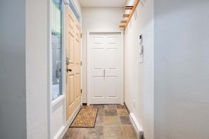 A narrow hallway with a white door, a glass door, and a doormat. - Large deck | Private Hot Tub | BBQ | Pet friendly (Whistler)