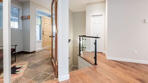 Un pasillo con puerta de madera, baranda de vidrio y piso de baldosas.
