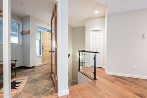 A hallway with a wooden door, a glass railing, and a tiled floor. - Large deck | Private Hot Tub | BBQ | Pet friendly (Whistler)