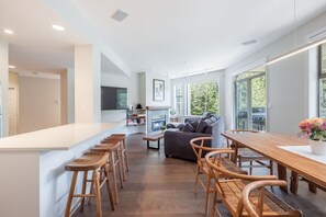 Une cuisine moderne dotée d’un îlot central, de tabourets de bar, d’une table à manger avec des chaises, d’un canapé et d’une cheminée.