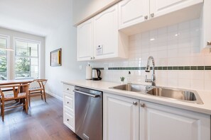 A modern kitchen with white cabinetry, stainless steel appliances, and a view of the outdoors through large windows. - Large deck | Private Hot Tub | BBQ | Pet friendly (Whistler)