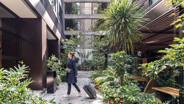 A modern building with a courtyard featuring potted plants and a person with a suitcase. - San Luis by Kukun Apartments (Ciudad de México)