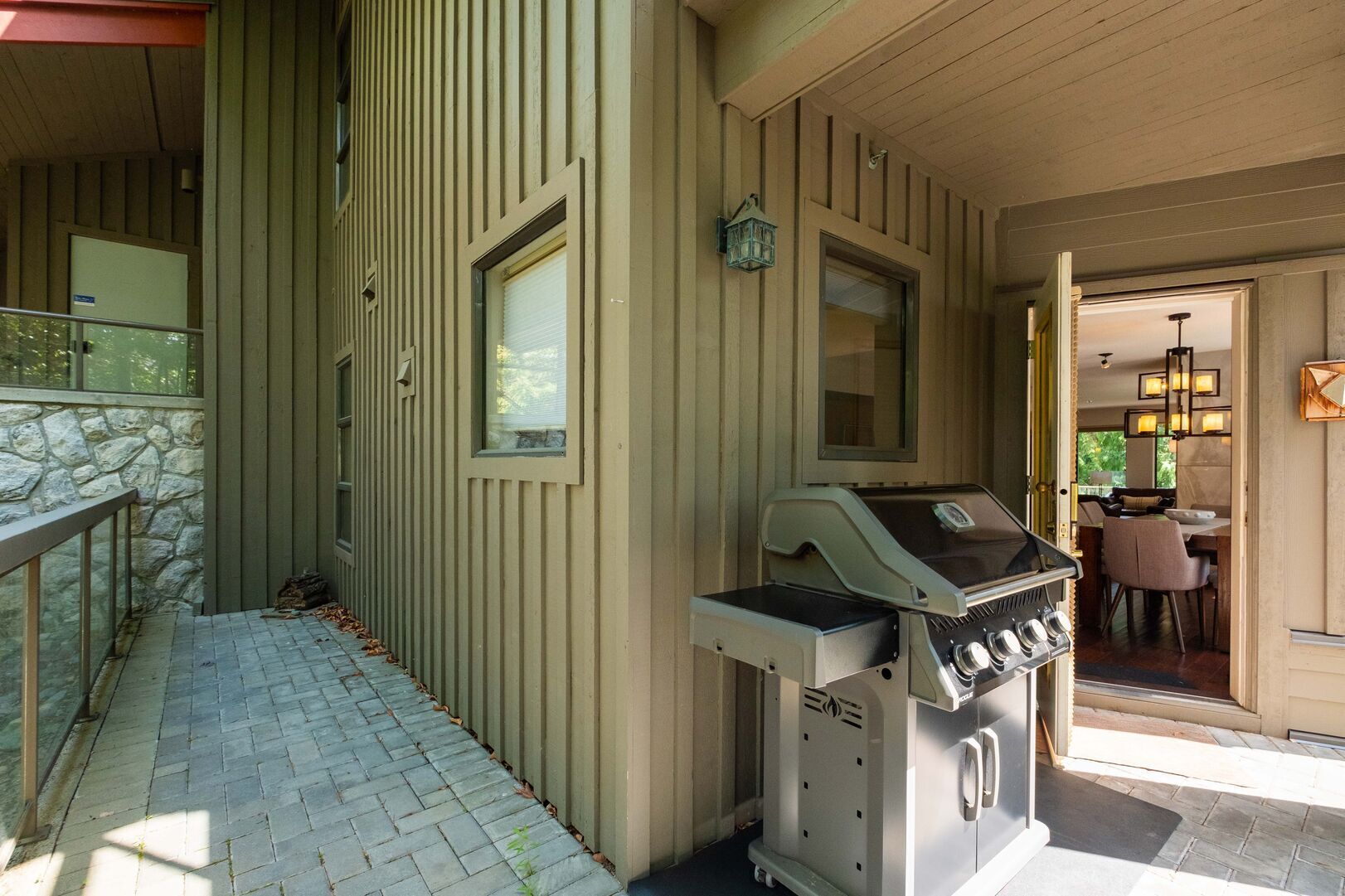 A covered outdoor area with a grill, stone wall, and a view into a dining area.