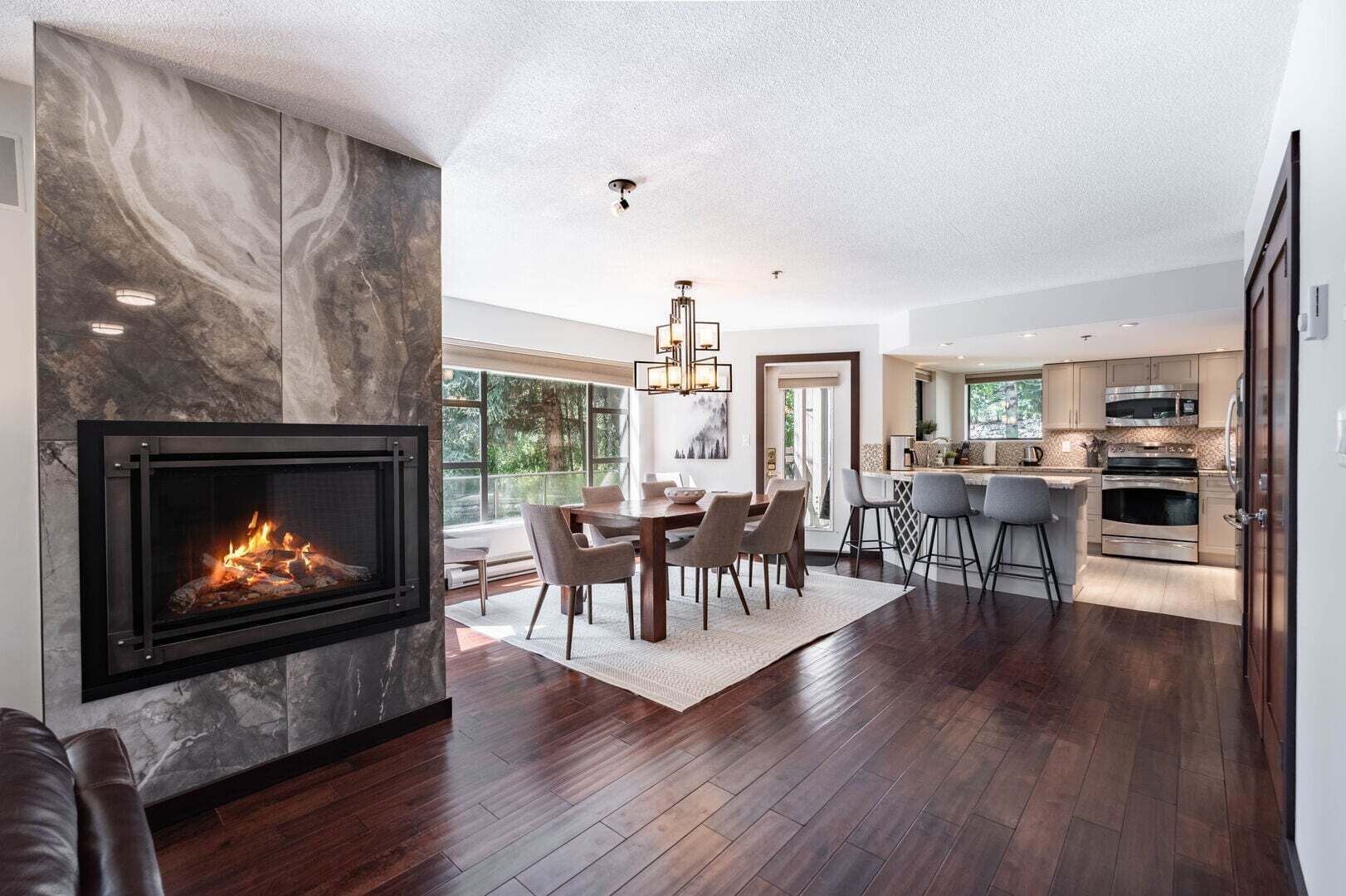 Ein modernes Interieur mit Kamin, Essbereich, Küche und großen Fenstern.