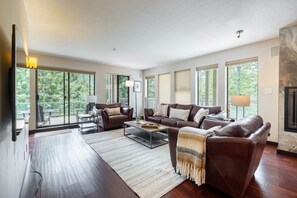 A spacious living room with a large window, a fireplace, and a cozy seating area. - Large patio | BBQ | Hot tub | Free parking (Whistler)