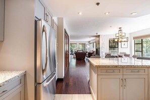 A modern kitchen with a large island, stainless steel appliances, and a dining area with a view. - Large patio | BBQ | Hot tub | Free parking (Whistler)