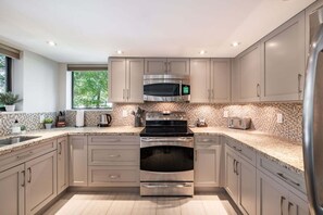A modern kitchen with stainless steel appliances, light-colored cabinetry, and a tiled backsplash. - Large patio | BBQ | Hot tub | Free parking (Whistler)