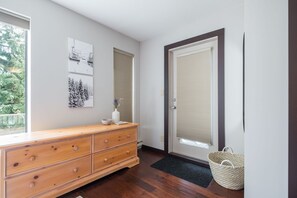 A hallway with a wooden dresser, two framed pictures, a door with a window, and a woven bag. - Large patio | BBQ | Hot tub | Free parking (Whistler)