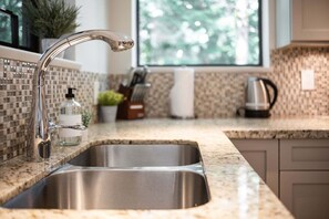 A kitchen with a stainless steel sink, a faucet, a window, and a countertop with a plant and a coffee maker. - Large patio | BBQ | Hot tub | Free parking (Whistler)