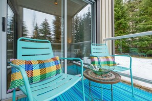 A balcony with two turquoise chairs, one with a colorful cushion and the other with a patterned cushion, and a small round table with a glass bowl. - Stunning 2 BDR | Steps to Blackcomb | Free Parking | Shared hot tub (Whistler)