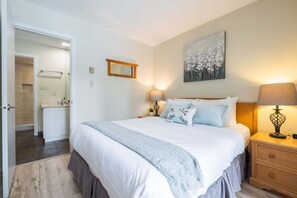 Ein Schlafzimmer mit einem großen Bett, Nachttischlampen, einem Bild an der Wand und einem durchgegangenen Tür erkennbaren Badezimmer.