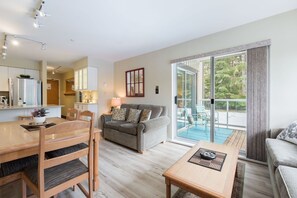Ein modernes Wohnzimmer mit einer Couch, einem Esstisch und Stühlen. Eine Glastür führt zu einem Balkon mit Gartenmöbeln.