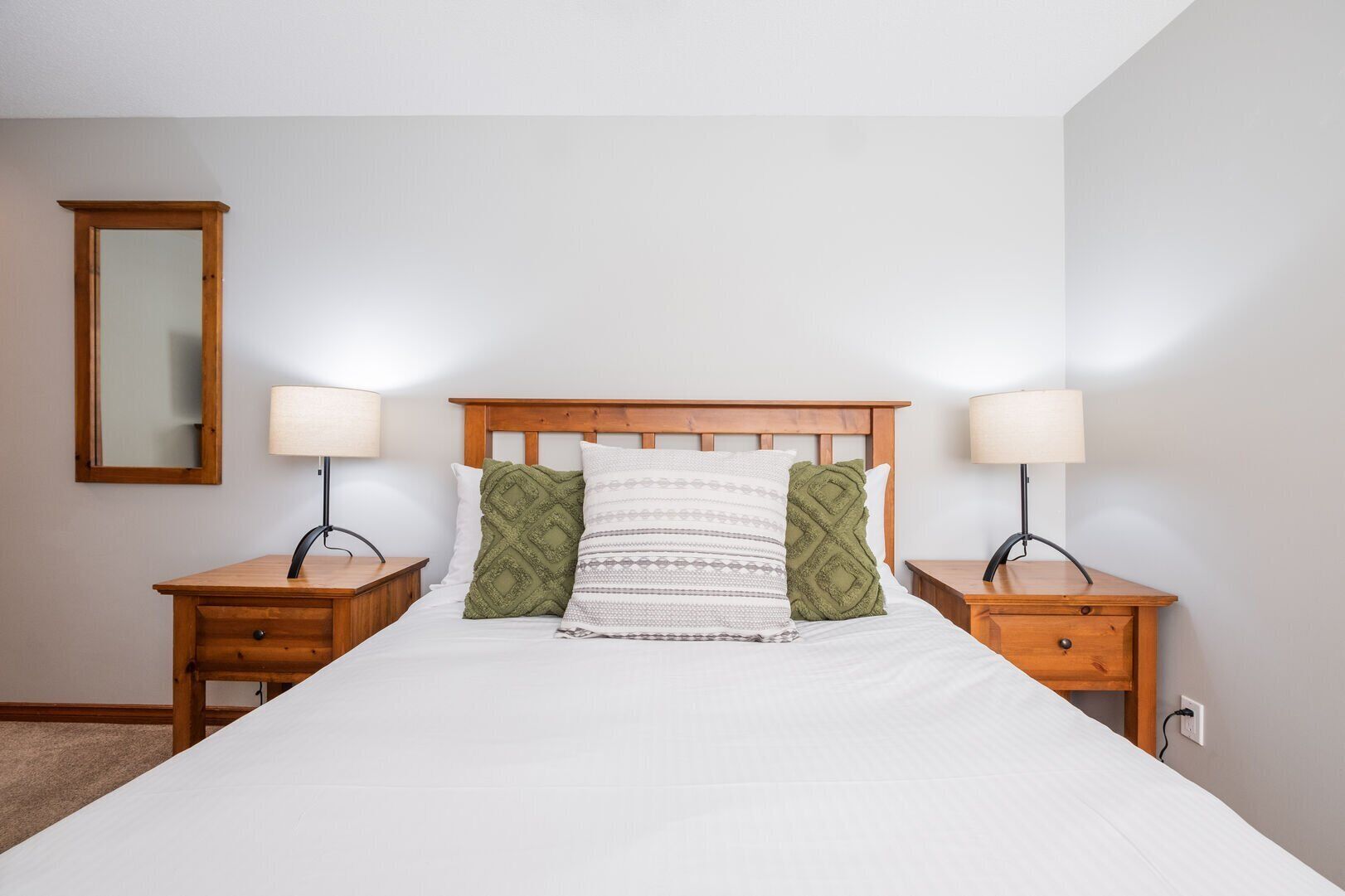 A neatly made bed with two bedside tables, each with a lamp, in a simple room with a wooden headboard.
