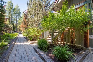 Un chemin pavé mène à un bâtiment entouré d’une clôture en bois et sur lequel est apposée une pancarte indiquant la présence d’un espace sauna.