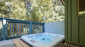 Un bain à remous sur une terrasse en bois avec une rambarde bleue, entouré d’arbres.