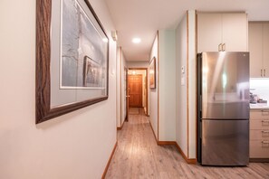A hallway with wooden flooring, a stainless steel refrigerator, and framed artwork on the walls. - Close to Blackcomb skiing | Private hot tub | BBQ (Whistler)