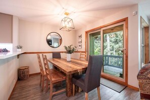 Un coin repas avec une table en bois, des chaises, un vase de fleurs, un miroir et une vue sur un balcon agrémenté de verdure.