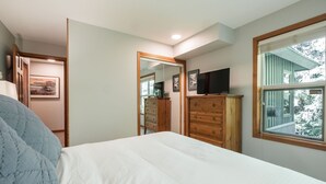 Une chambre à coucher comprenant un lit, une commode, un téléviseur et une fenêtre donnant sur des arbres.