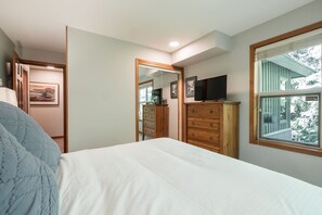A bedroom with a bed, dresser, television, and a window with a view of trees. - Close to Blackcomb skiing | Private hot tub | BBQ (Whistler)