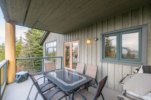 A covered outdoor area with a glass table and chairs, a grill, and a view of trees. - Pets | BBQ | Sundeck | Private garage | Ski-in/out (Whistler)
