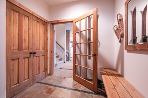 A hallway with wooden doors, a glass door, a bench, and a staircase in the background. - Pets | BBQ | Sundeck | Private garage | Ski-in/out (Whistler)