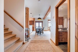 A staircase leading to a dining area with a table and chairs, a kitchen with wooden cabinets, and a large window. - Pets | BBQ | Sundeck | Private garage | Ski-in/out (Whistler)