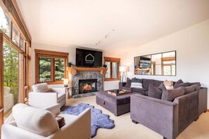 A spacious living room with a fireplace, large windows, and a modern fireplace mantel. - Pets | BBQ | Sundeck | Private garage | Ski-in/out (Whistler)