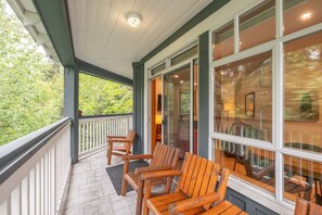 Eine überdachte Veranda mit Holzstühlen und Blick ins Innere durch Glastüren, sowie ein Steinboden.