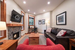 Ein gemütliches Wohnzimmer mit Kamin aus Stein, einer Ledersofa, einem Holztisch und einem flachbildfernseher, der über dem Kamin befestigt ist.