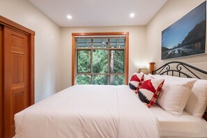 Um quarto com uma cama grande, uma janela com vista para árvores, uma porta de madeira e um quadro na parede.