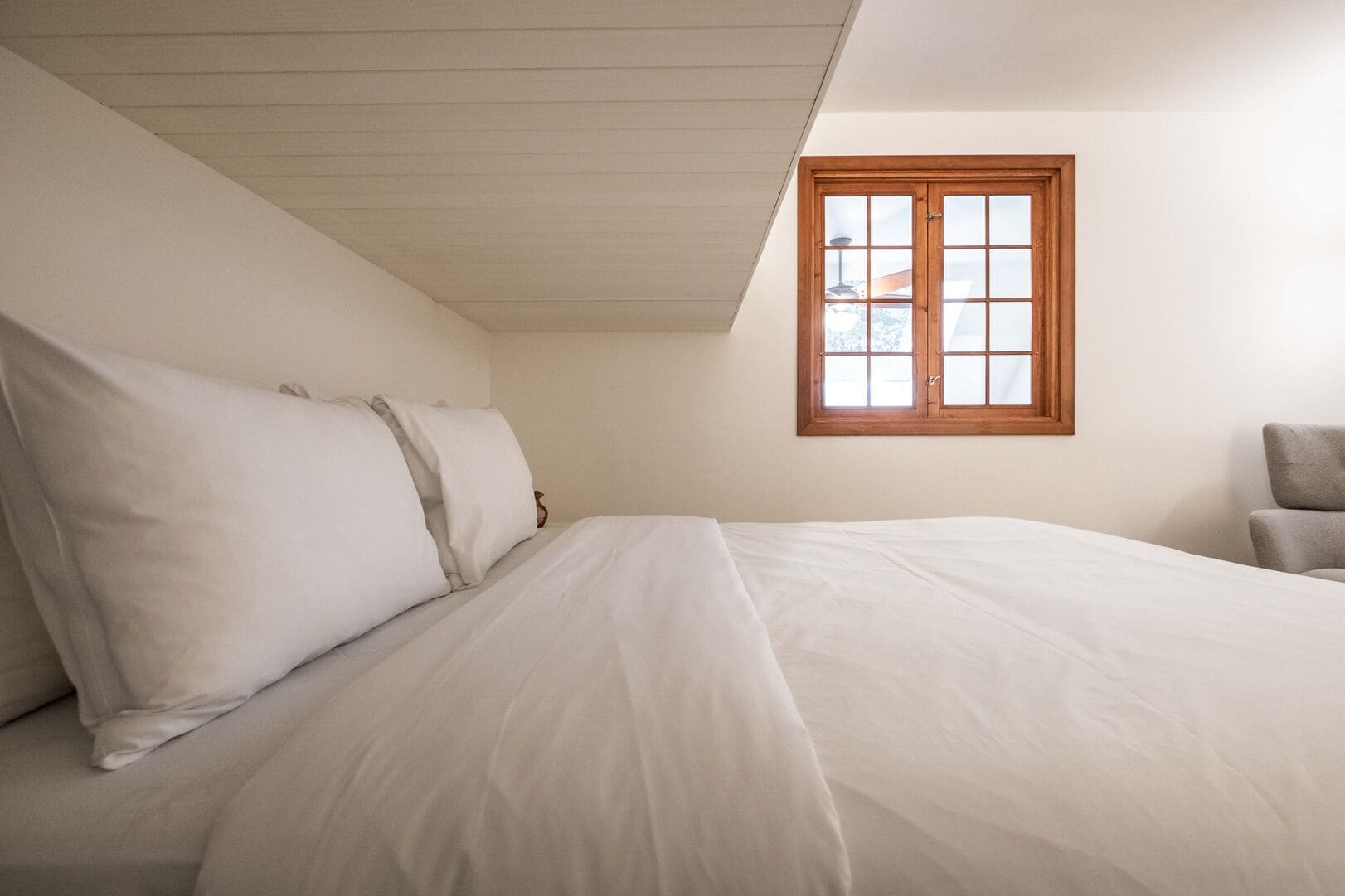 A bedroom with a bed, pillows, a window, and a chair.
