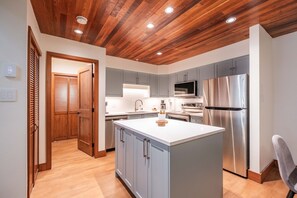 A modern kitchen with a wooden ceiling, grey cabinets, stainless steel appliances, and a central island. - Pet friendly | Renovated | Free parking | Spacious (Whistler)