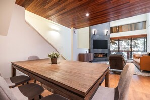 A modern interior with a wooden dining table, a fireplace, and a large window offering a view of trees. - Pet friendly | Renovated | Free parking | Spacious (Whistler)